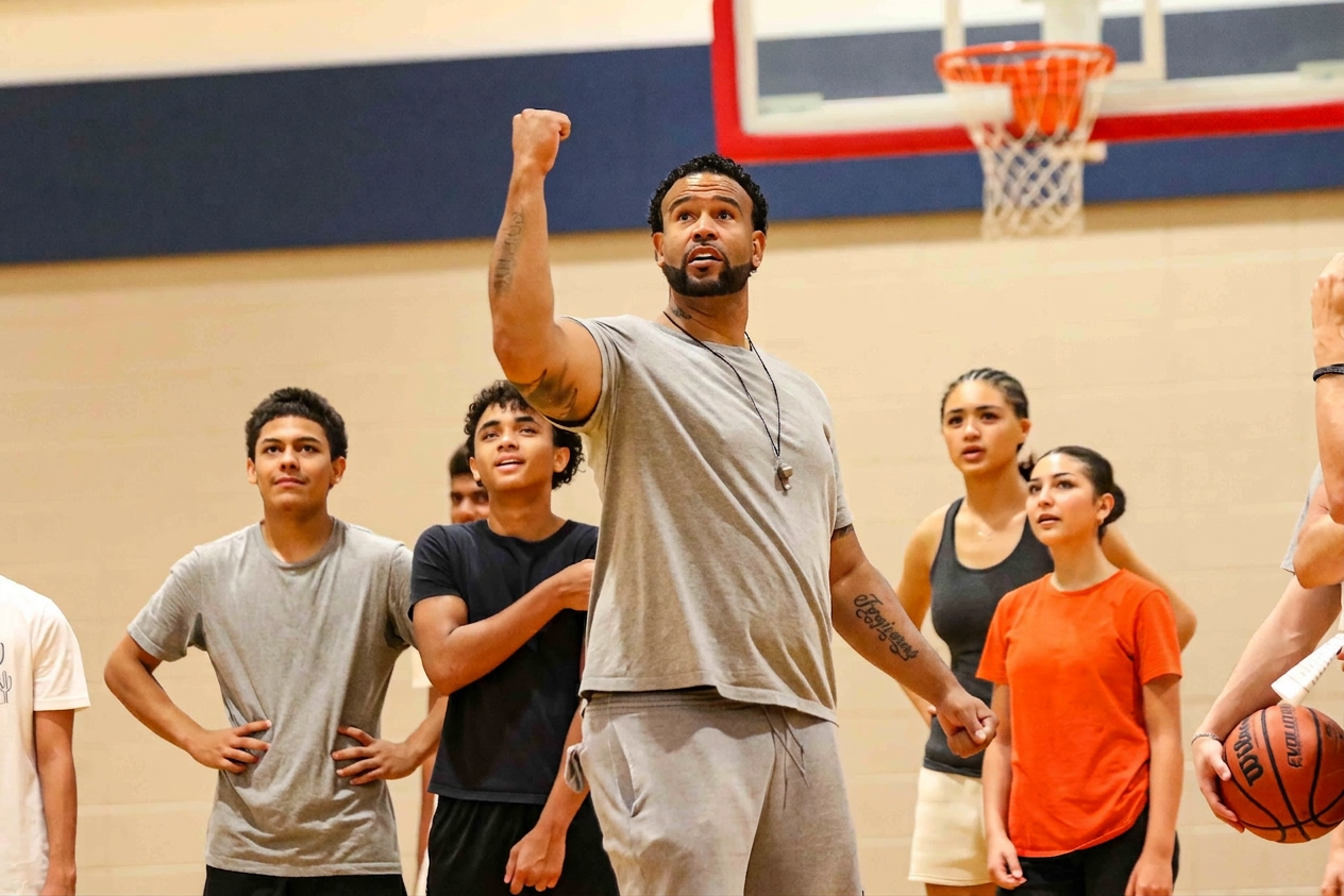 Coach CJ leading a drill, fist raised, with young athletes watching